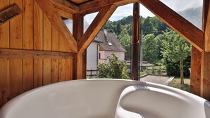 A wooden cabin with a large bathtub and a view of a house and trees. - Chalet du Tanet in Soultzeren for 7 people spa sauna (Soultzeren)