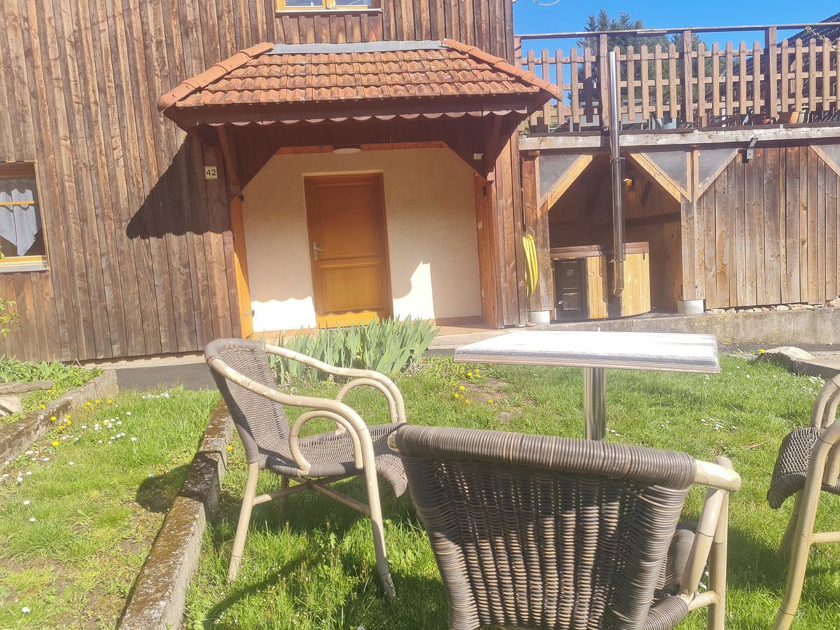 A wooden building with a tiled roof, a small porch, and a table with chairs.
