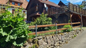 A traditional wooden house with a balcony, surrounded by greenery and a stone wall. - Chalet du Tanet in Soultzeren for 7 people spa sauna (Soultzeren)