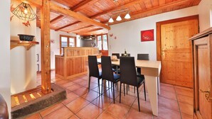 A rustic interior with a wooden ceiling, a dining area with black chairs, and a kitchen in the background. - Chalet du Tanet in Soultzeren for 7 people spa sauna (Soultzeren)