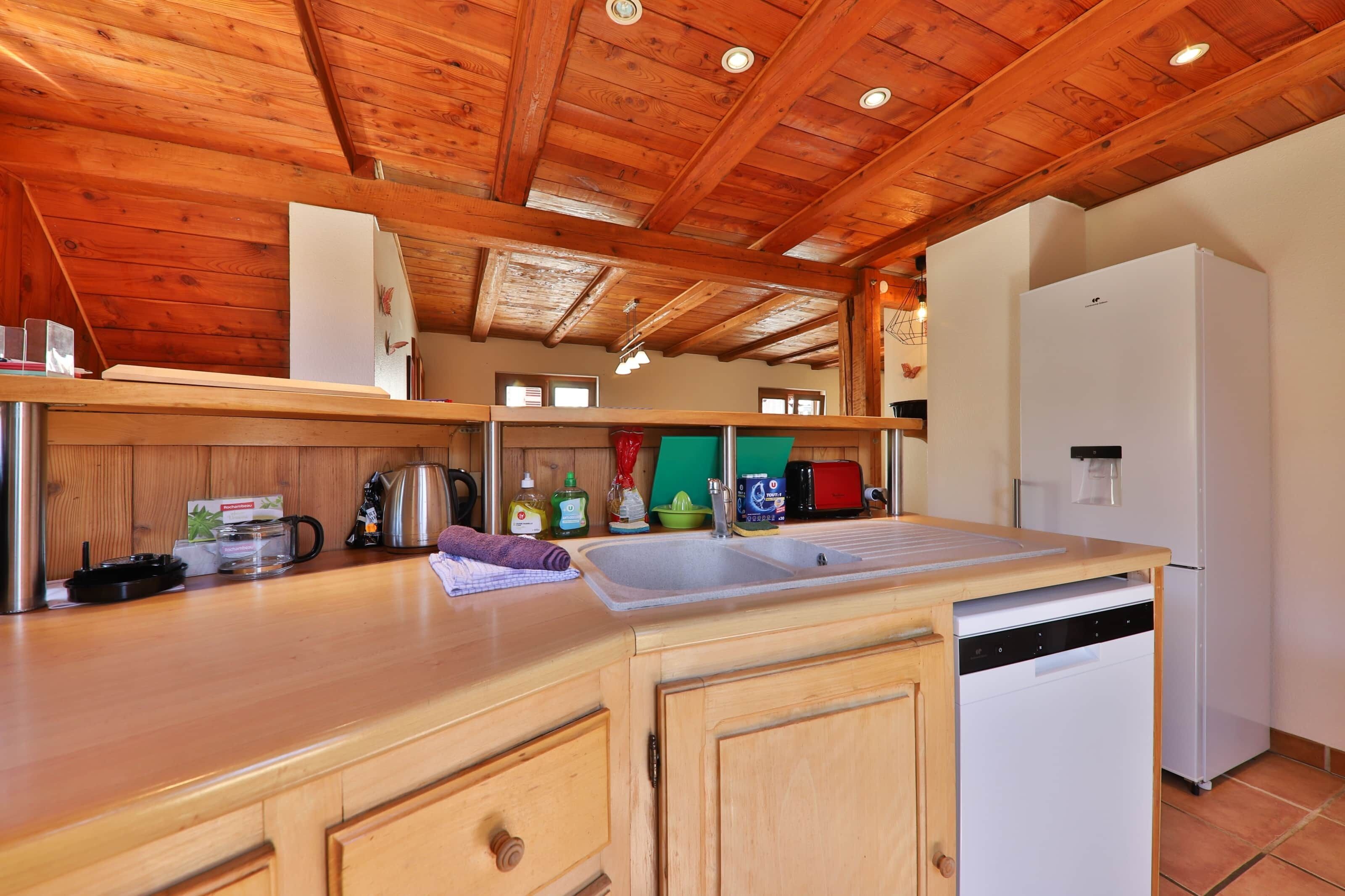 A kitchen with wooden ceiling beams, a white refrigerator, a sink, and various kitchen appliances.