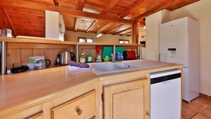 A kitchen with wooden ceiling beams, a white refrigerator, a sink, and various kitchen appliances. - Chalet du Tanet in Soultzeren for 7 people spa sauna (Soultzeren)