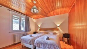 Une chambre avec deux lits, un plafond en bois, une fenêtre avec des rideaux, un radiateur et un luminaire fixé au mur.