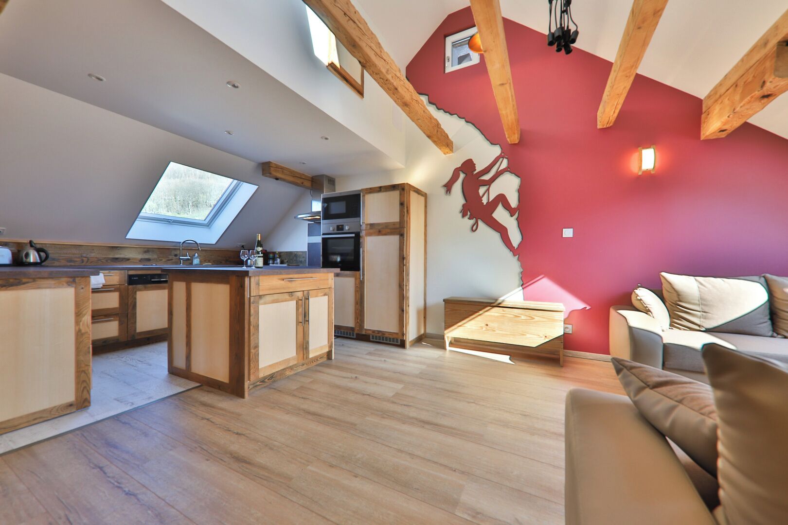 A modern kitchen with wooden cabinets, a skylight, and a red accent wall.