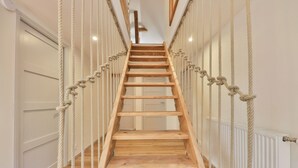 A wooden staircase with rope railings, leading to a landing with a door and a radiator. - Luxurious 500 m² villa with vaulted cellar, sauna, spa, large outdoor spaces (Sondernach)