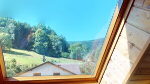 A view from a wooden-framed window overlooking a green landscape with trees and a house. - Gîte Familial Alsace 11 pers - BBQ & Panoramic View (Sondernach)