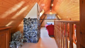 A wooden interior with a stone wall, a red chair, and a wooden railing. - Gîte Familial Alsace 11 pers - BBQ & Panoramic View (Sondernach)