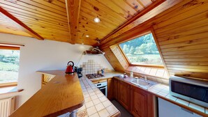 A kitchen with wooden cabinets, a stove, and a window overlooking a green landscape. - Gîte Familial Alsace 11 pers - BBQ & Panoramic View (Sondernach)