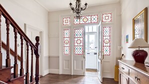 Una escalera de madera que conduce a una habitación con un candelabro, una alfombra estampada y una puerta con vidrieras.