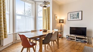 Un comedor con una mesa de madera, sillas y un televisor sobre un mueble.
