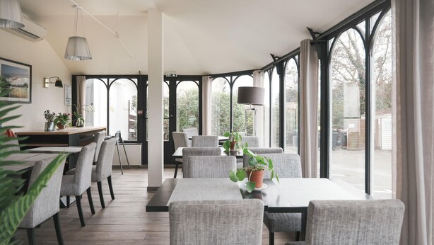 A dining area with a long table and chairs, potted plants, and a view through large windows. - BRIT HOTEL CONFORT ORLY MORANGIS (Morangis)