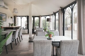 A dining area with a long table and chairs, potted plants, and a view through large windows. - BRIT HOTEL CONFORT ORLY MORANGIS (Morangis)