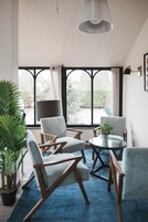 Una sala de estar moderna con ventanas amplias, una mesa redonda de vidrio y varias sillas.