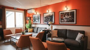 A modern lounge area with a sofa, chairs, and a coffee table. There are framed pictures on the wall and a potted plant on the table. - BRIT HOTEL CONFORT ORLY MORANGIS (Morangis)