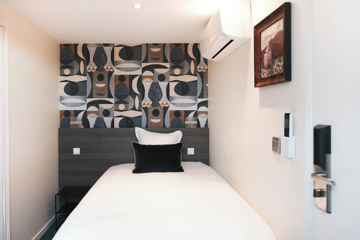 A modern hotel room with a large bed, a patterned wall, a painting, and a small table.