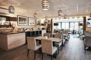 Un restaurante con mostrador de madera, varias mesas y sillas. Hay lámparas colgantes y cuadros en las paredes.