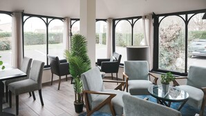 A modern lounge area with comfortable seating, large windows, and a potted plant. - BRIT HOTEL CONFORT ORLY MORANGIS (Morangis)