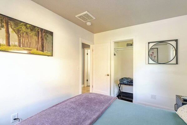 Un dormitorio con cama, armario, espejo y un cuadro en la pared.