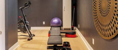 Un gimnasio en casa con banco, pelota de ejercicios, mancuernas y bicicleta estática.