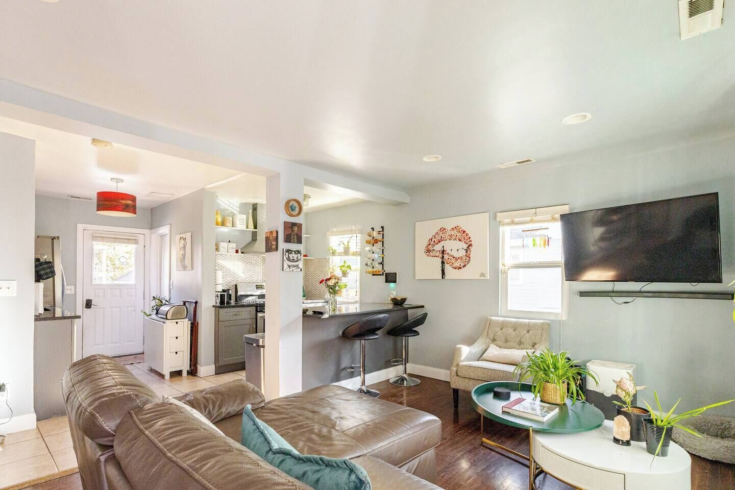 A modern living room with a sofa, a coffee table, and a TV. There is a kitchen in the background with a dining area.