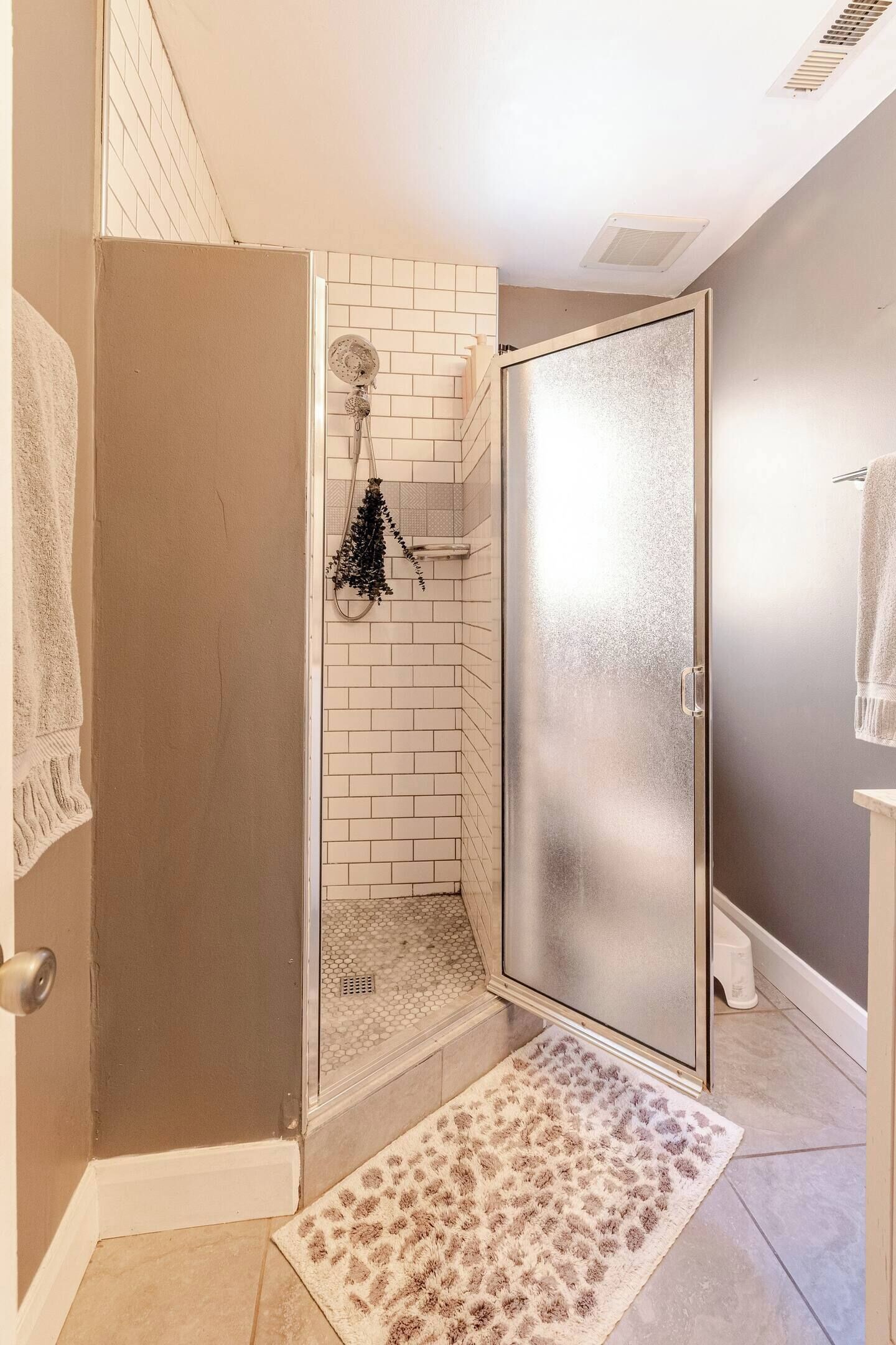 A shower area with a glass door, a white tiled shower wall, a showerhead, and a towel rack.