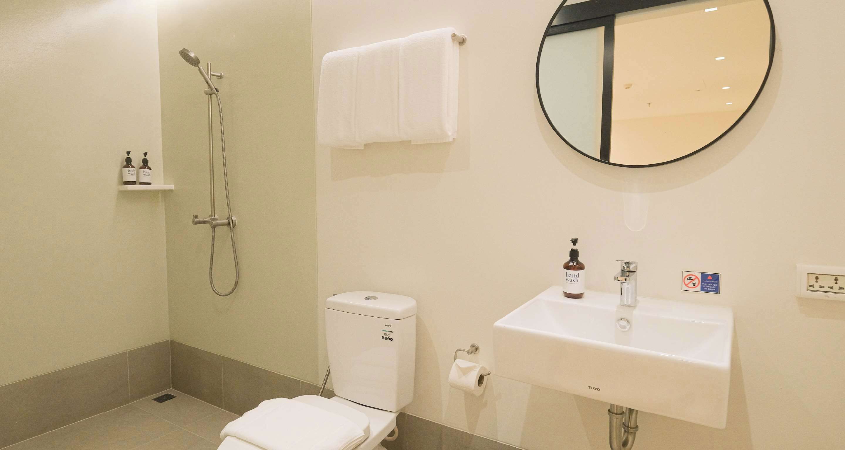 A bathroom with a toilet, a sink, a mirror, a shower, and a towel rack.