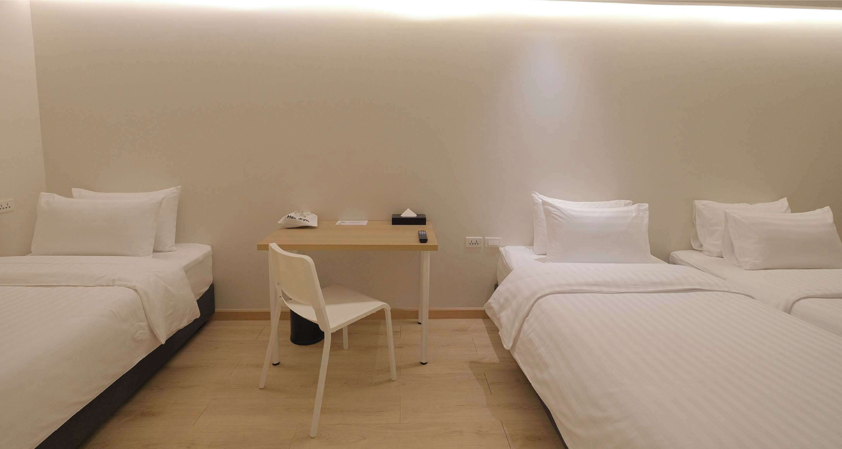 A hotel room with two beds, a desk, a chair, and a small table with a tissue box and remote control.