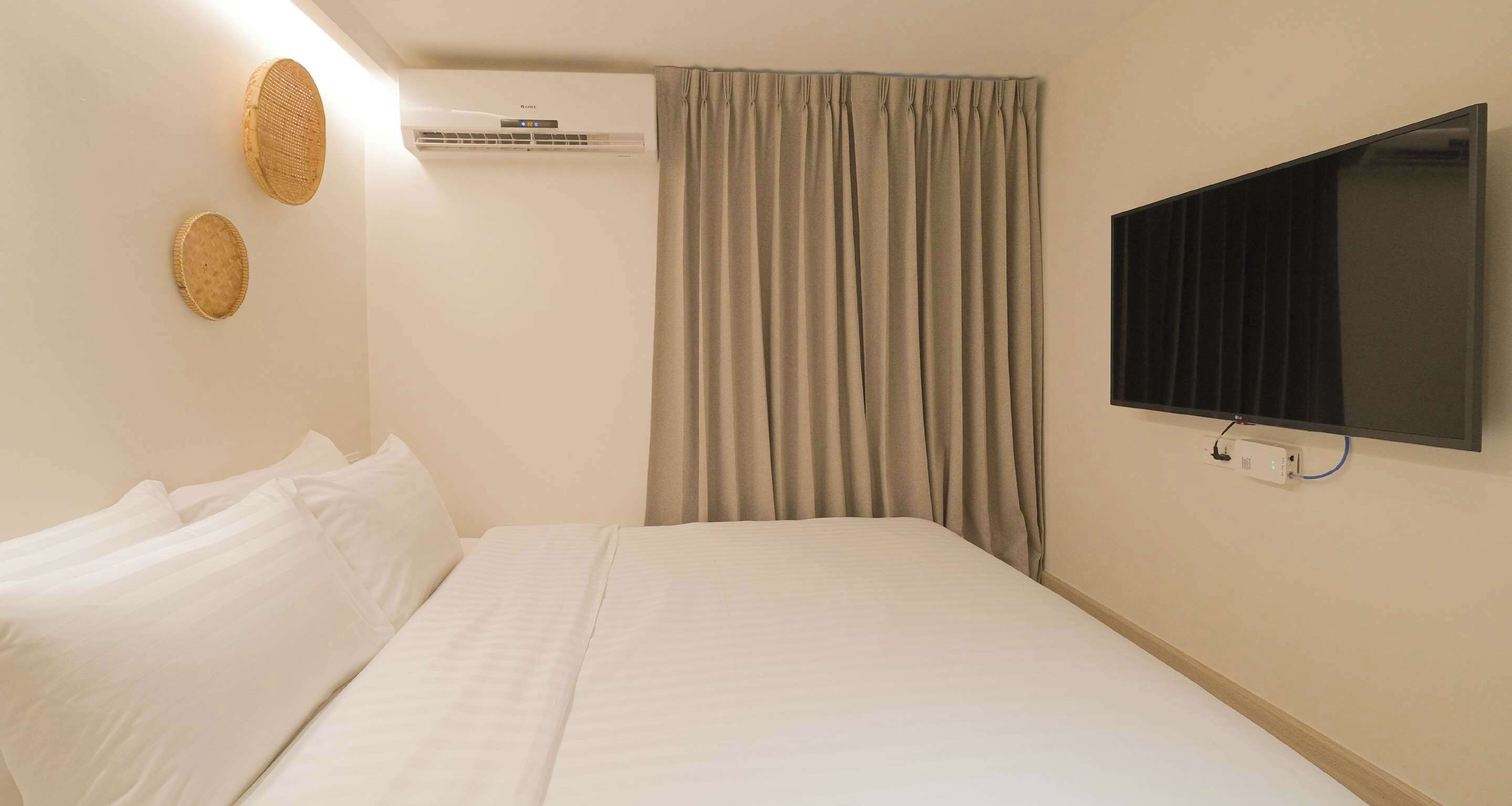 Une chambre d’hôtel équipée d’un lit, d’un appareil de climatisation, d’un téléviseur fixé au mur et d’un rideau.