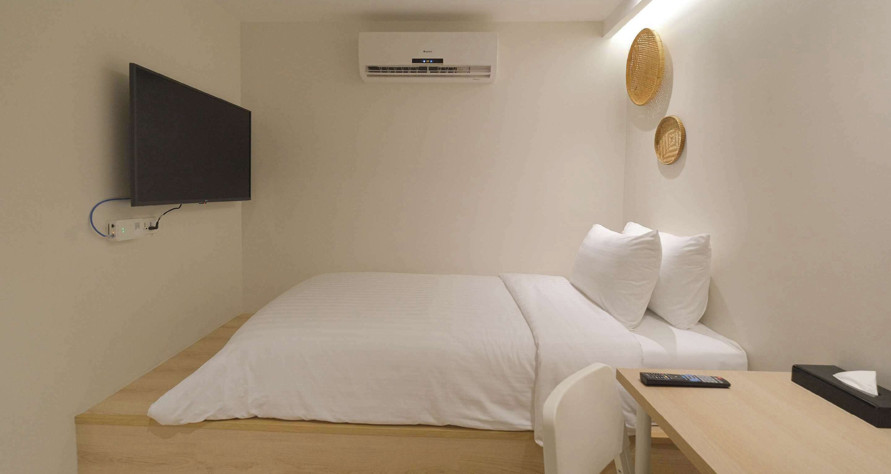 Una habitación con una cama, un escritorio, un televisor montado en la pared y un equipo de aire acondicionado.