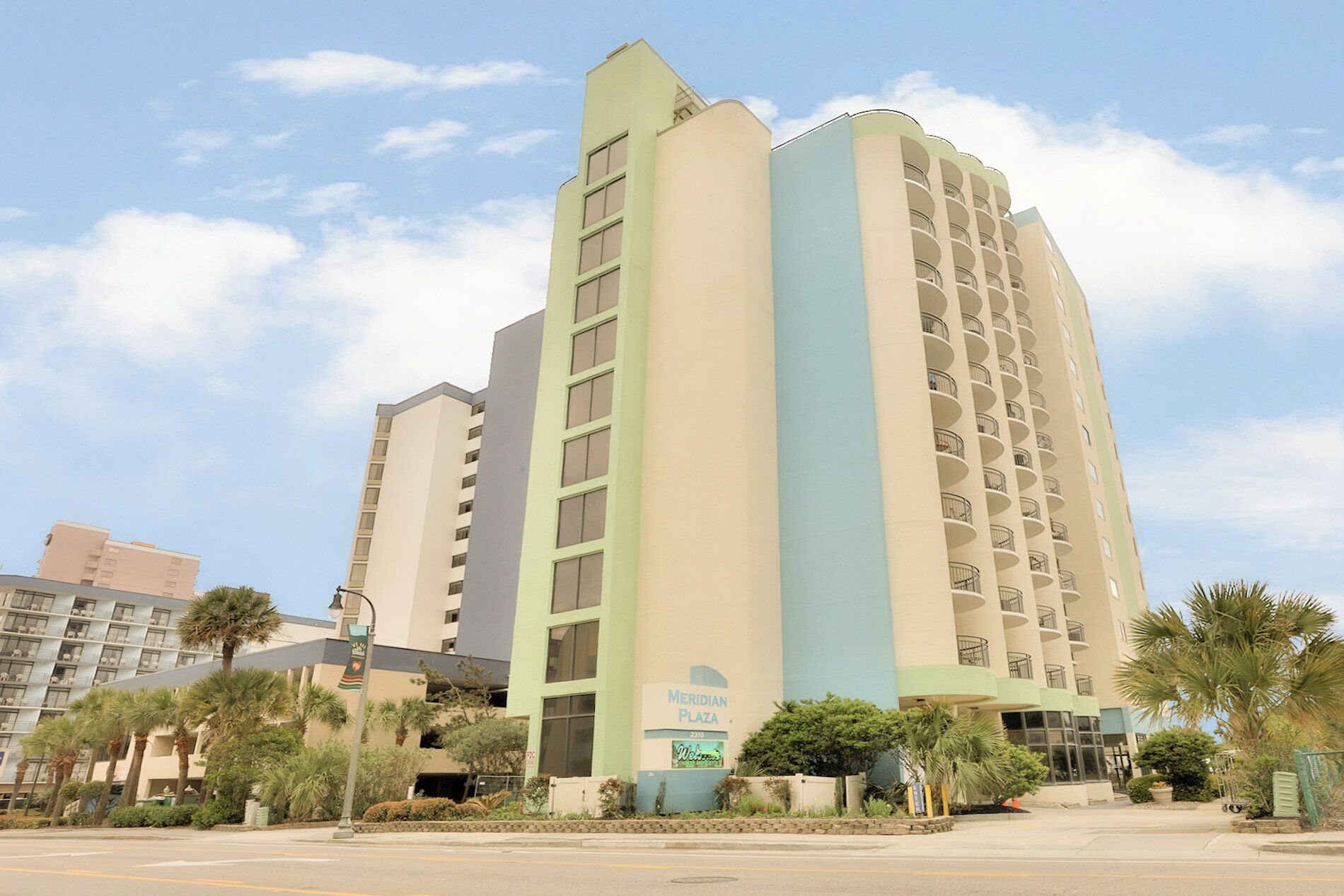 A multi-story hotel with a light green and beige facade, featuring a prominent vertical blue stripe.