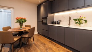 A modern kitchen with dark cabinets, a marble countertop, and a dining area with a wooden table and chairs.