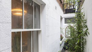 A narrow alleyway with a white building, a window with a plant inside, and a potted plant outside.