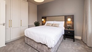 A bedroom with a large bed, a nightstand with a lamp, a wardrobe, and a ceiling light.