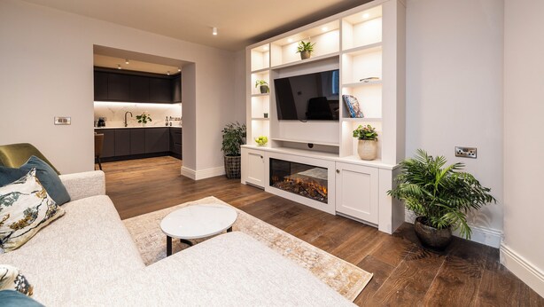 A modern living room with a sofa, a coffee table, and a fireplace. There is a kitchen in the background with a sink and cabinets.
