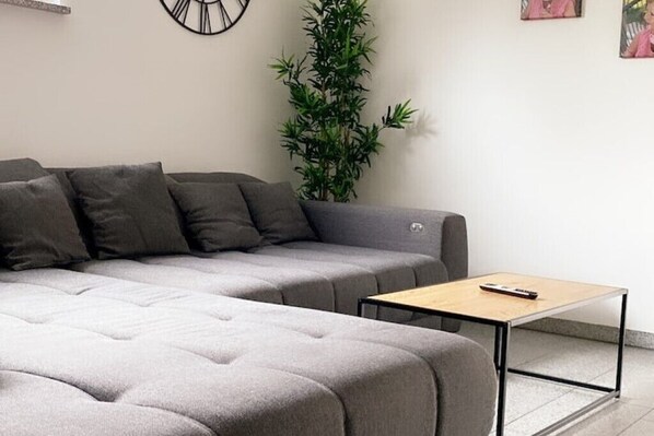 A modern living room with a grey sectional sofa, a small wooden coffee table, and a tall green plant.