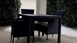 An outdoor dining area with a table and four chairs, surrounded by greenery.