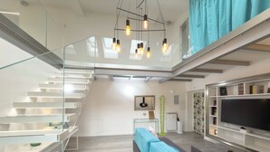 A modern living room with a glass staircase, a sofa, a flat-screen TV, and a bookshelf. - Luxury Vatican Penthouse with 2 terraces & hot-tub (Roma)