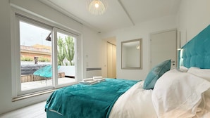 A bedroom with a large bed, a sliding glass door leading to an outdoor area with plants and a patio, and a modern ceiling light fixture. - Luxury Vatican Penthouse with 2 terraces & hot-tub (Roma)