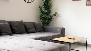 A modern living room with a grey sectional sofa, a small wooden coffee table, a tall green plant, and a wall clock.