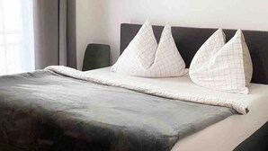 A neatly made bed with a dark headboard and white pillows with a grid pattern.