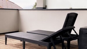 A balcony with a black wicker lounge chair and a small table.