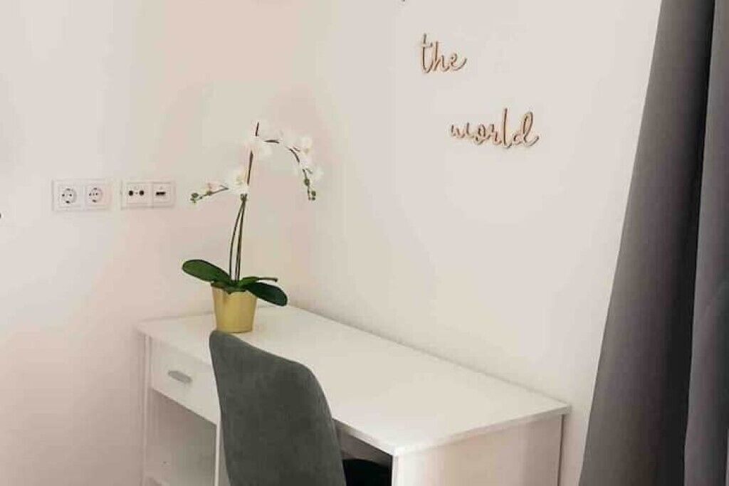 Et hvidt skrivebord med en grå stol, en lille potteplante og en væg med teksten "the world" i gylden skrift.