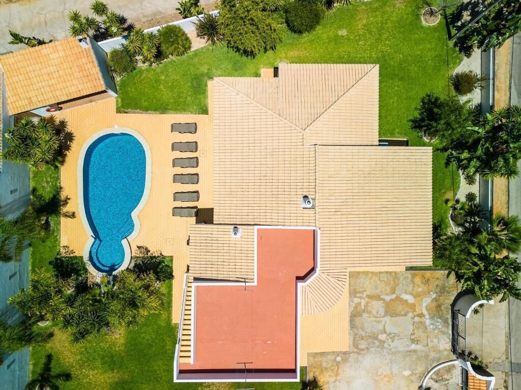 An aerial view of a property with a swimming pool, lounge area, and a large covered patio.