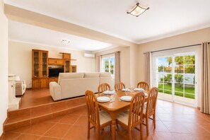 Un vaste espace de vie comprenant un canapé, une table à manger et des chaises, une cuisine équipée d’armoires et une vue dégagée grâce à de grandes portes coulissantes.