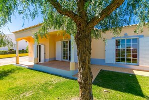 Relax on the covered patio surrounded by a lush lawn and a majestic tree.