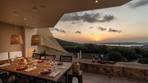 Un espace de restauration en plein air avec une table dressée pour quatre personnes, offrant une vue panoramique sur un paysage magnifique et un coucher de soleil.