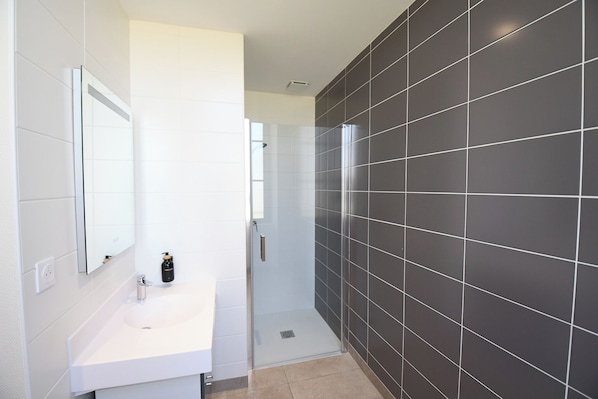 Ein modernes Badezimmer mit einem weißen Waschbecken, einem Spiegel und einer Duschkabine.