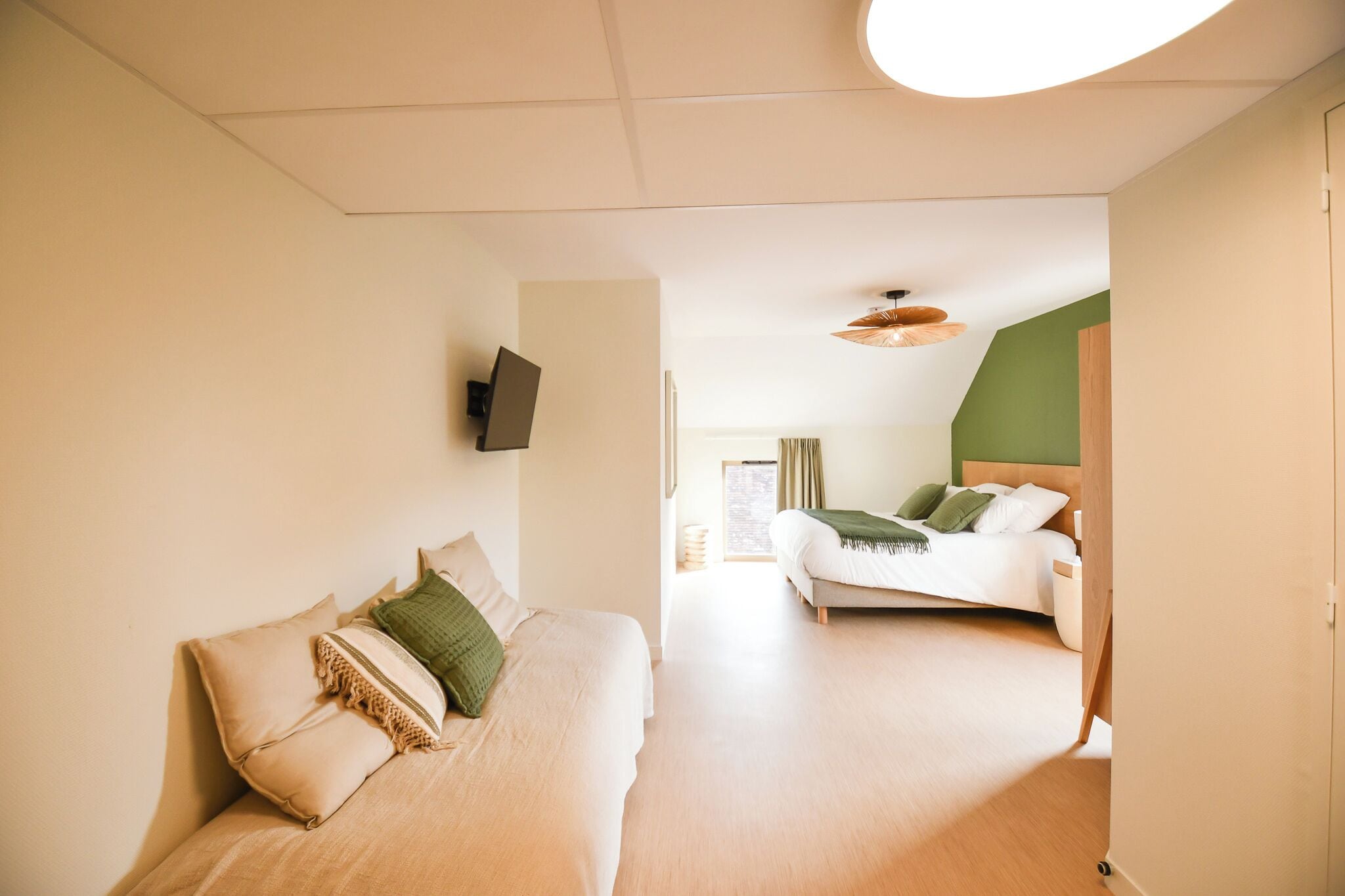 Une chambre d’hôtel moderne équipée d’un canapé-lit, d’un lit séparé et d’un téléviseur à écran plat fixé au mur.