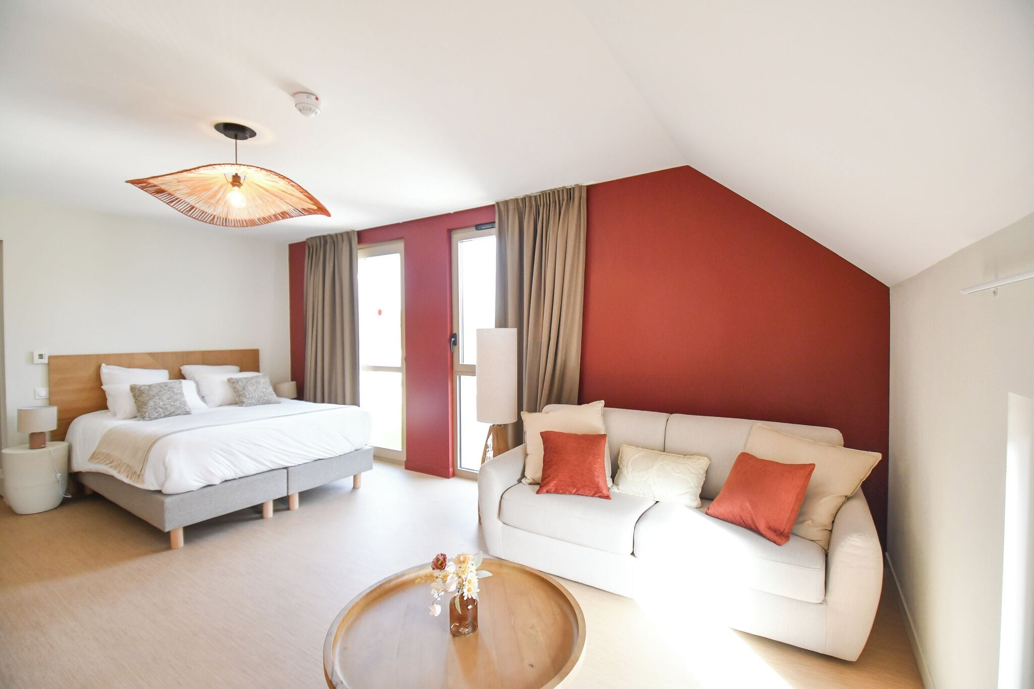 Quarto de hotel moderno com cama, sofá, mesa de centro e ventoinha no teto.