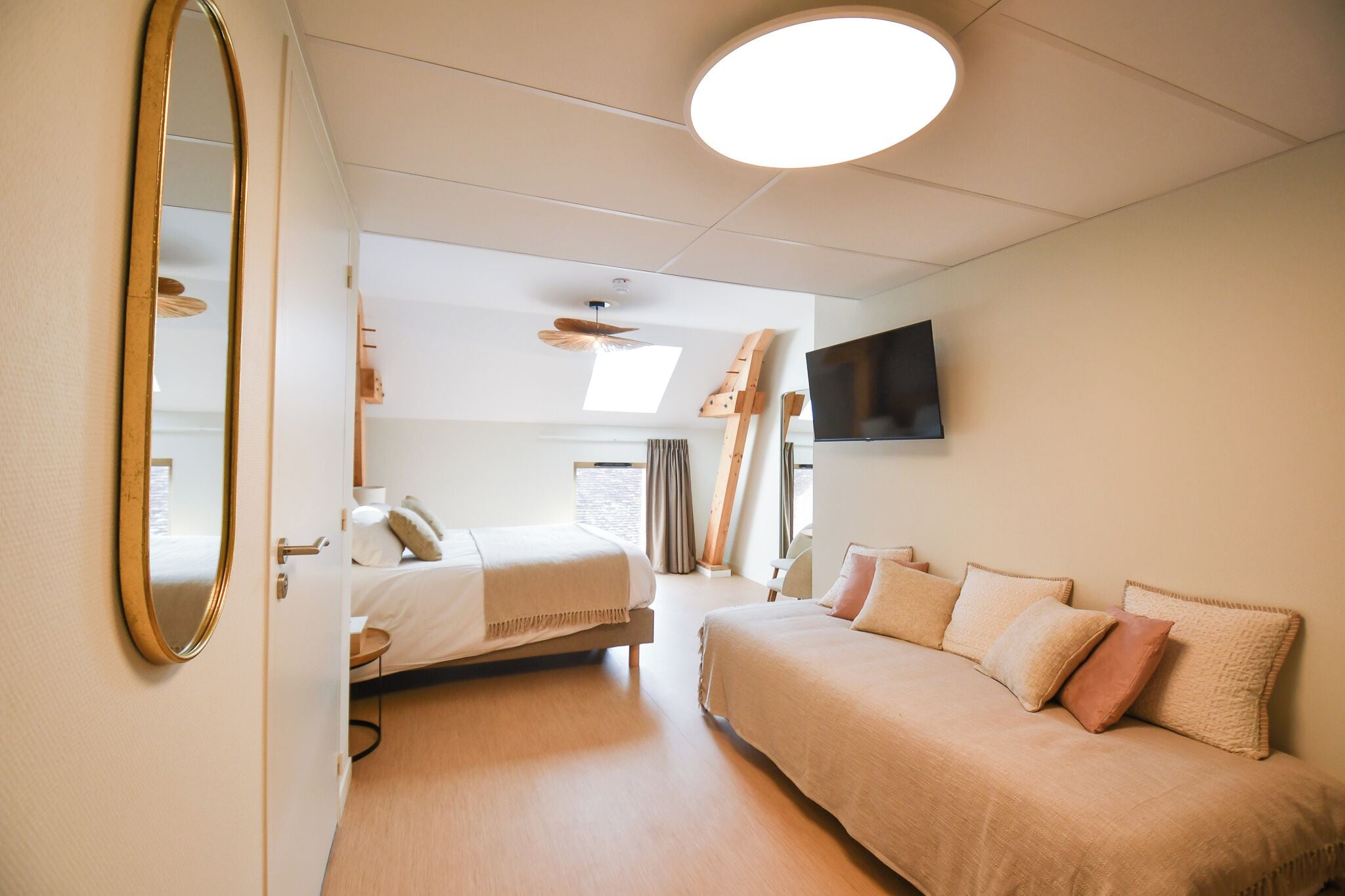 Et hotelværelse med en seng, en sofa, et fjernsyn monteret på væggen og en ventilator i loftet.